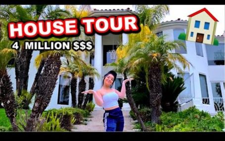 dani standing infront of her big mansion spreading her hands 